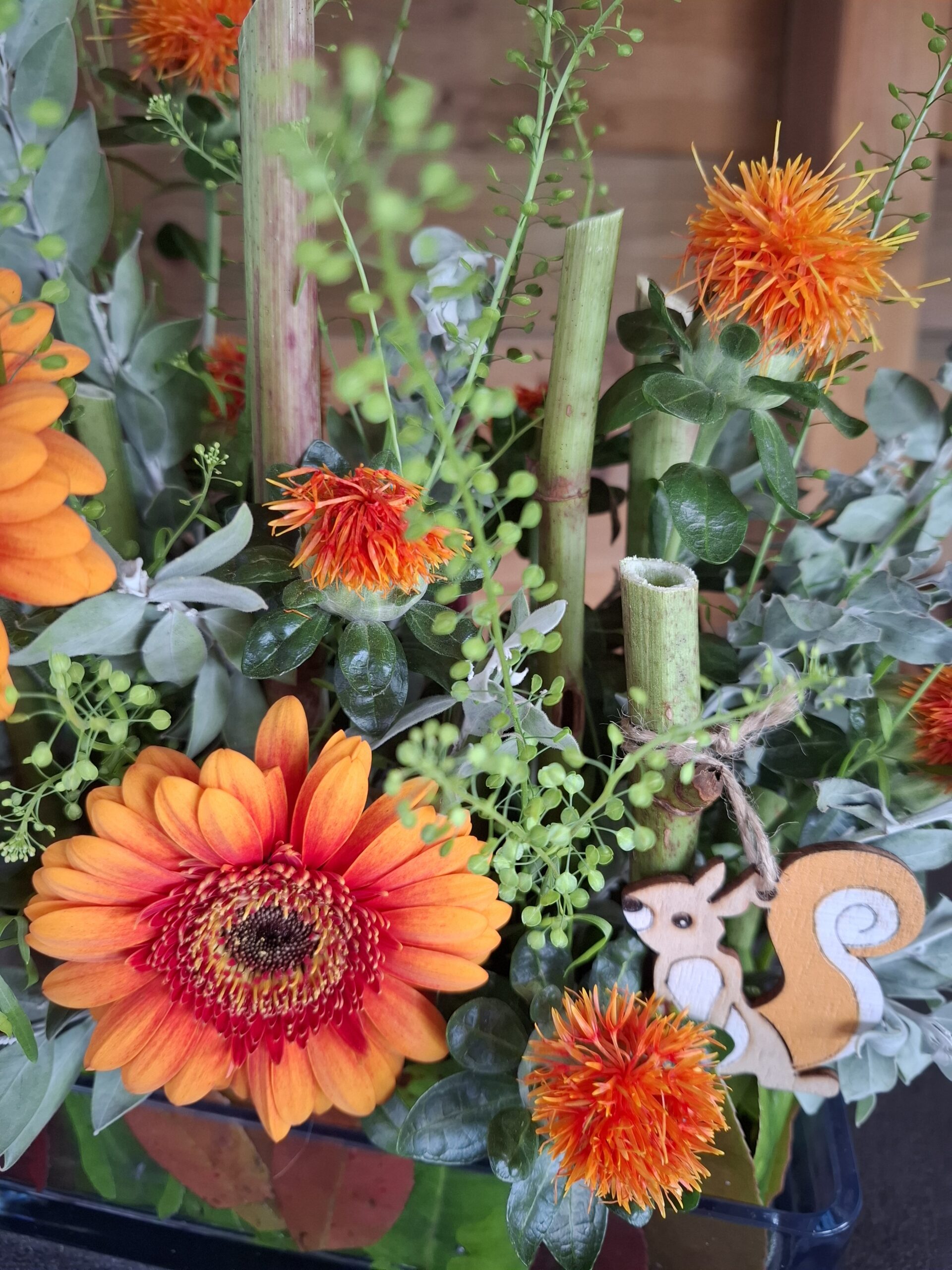 Floral workshop bouquet with large orange flowers, green foliage and small wood squirrel decoration, warm floral composition.