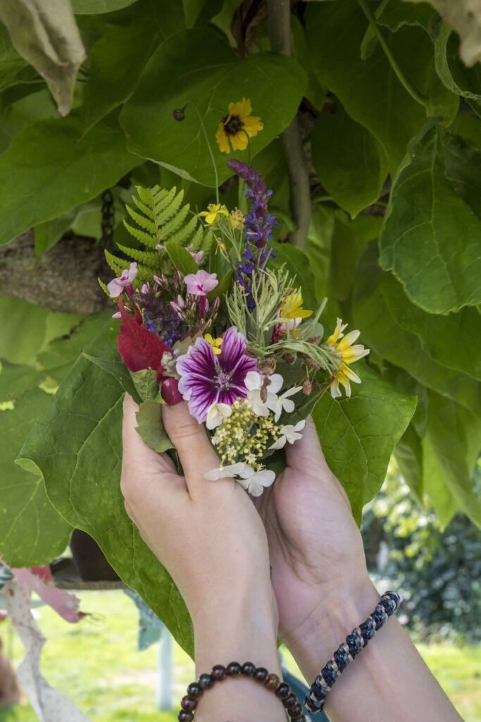  Mains d’une participante tenant un petit bouquet sauvage coloré devant un feuillage vert, illustration de l’atelier floral créatif et détente. 